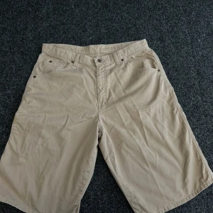 Beiga shorts från Polo Jeans Company - Snygga beiga shorts från Polo Jeans Company med klassisk femficksdesign och knappgylf. Tillverkade i bomull och har en avslappnad passform. Perfekta för varma dagar och enkel att matcha med det mesta.