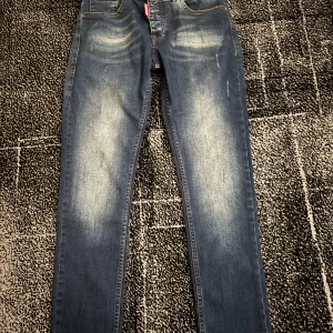 Blå jeansbyxor från Dsquared2 - Snygga blå jeansbyxor från Dsquared2 med klassisk femficksdesign och diskreta slitningar framtill. Jeansen har raka ben och normal passform, perfekt för en stilren look. Tydlig röd Dsquared2-lapp bak i midjan.