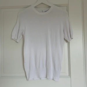 Vit tröja  med knappar - Säljer en vit tröja med korta ärmar och tre knappar bak. Tröjan har en klassisk och enkel design som passar till mycket. Perfekt för dig som gillar stilrena plagg med en twist.