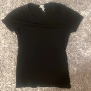 Svart basic t-shirt - En enkel svart t-shirt med rund halsringning och korta ärmar. Perfekt att matcha med jeans eller shorts för en clean och stilren look. T-shirten har en klassisk passform och är tillverkad i mjukt material.