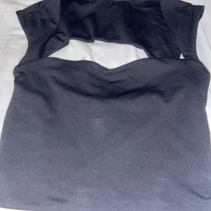 Svart croppad topp från SHEIN - Säljer en svart croppad topp från SHEIN med öppen rygg  i storlek XS. Toppen har en unik cut-out detalj upptill och är tillverkad i ett stretchigt syntetmaterial.  
