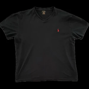 Svart v-ringad t-shirt från Polo Ralph Lauren - Säljer en svart v-ringad t-shirt från Polo Ralph Lauren med den klassiska röda broderade loggan på bröstet. T-shirten har korta ärmar och är tillverkad i mjuk bomull. Perfekt för en stilren och enkel look. Mer info i dm