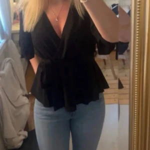 Svart omlottblus - Snygg svart omlottblus med knytband i midjan och korta puffärmar. Ser ut som ett band runt midjan i bilden men det är det inte💓