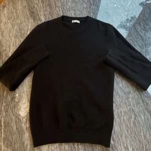 Svart stickad tröja med rund hals - En klassisk svart stickad tröja med rund halsringning och långa ärmar. Perfekt basplagg som passar till många olika stilar. Tröjan har en diskret struktur i materialet och ribbade muddar vid ärmslut och nederkant.