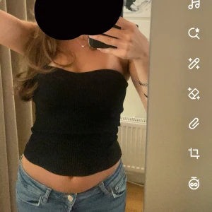 Svart ribbad tubtopp - Säljer en svart ribbad tubtopp med stretchigt material. Toppen kan både bäras armlös och med armar och sitter tight mot kroppen, perfekt till jeans eller kjol. Enkel och stilren design utan synliga detaljer.