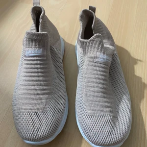 Beige stickade sneakers från Sprandi - Säljer ett par beige stickade sneakers från Sprandi med vit sula. Skorna har en slip-on design utan snörning och är tillverkade i ett luftigt, stickat material som ger en sportig och modern look.