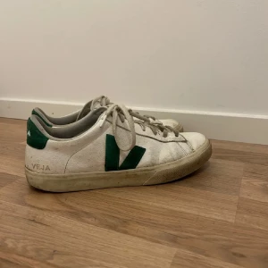 Veja skor  - Säljer ett par klassiska vita Veja sneakers med gröna detaljer och snörning. Skorna har en platt sula och rund tå, perfekt för en stilren vardagslook. Ikonisk V-logga på sidan och bekväm innersula.