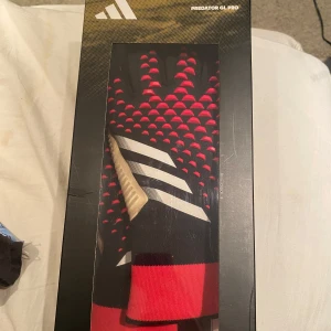 Adidas Predator GL Pro målvaktshandskar - Säljer ett par Adidas Predator GL Pro målvaktshandskar i svart, rött och beige med vita detaljer. Handskarna har greppvänlig insida och elastisk mudd. Perfekta för fotbollsmålvakter som vill ha bra kontroll och stil på planen. Använda fåtal gånger och funkar felfritt Nypris 1300kr