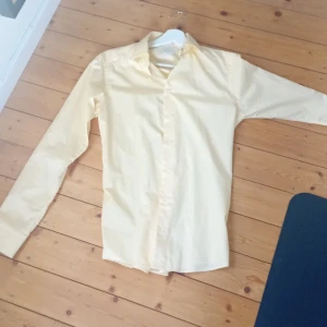 Ljusgul skjorta från Eton - Säljer en stilren ljusgul skjorta från Eton i slim fit. Skjortan har långa ärmar, klassisk krage och knäppning framtill. Perfekt för dig som vill ha en fräsch och elegant look med en touch av färg. Saknas ett knapp hål på ena ärmen