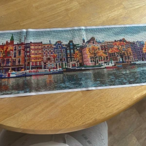 Diamond painting-bild av stad vid kanal - Säljer en färgglad diamond painting-bild som föreställer en stad med höghus och träd längs en kanal. Bilden har många detaljer och klara färger, med reflektioner i vattnet. Perfekt för dig som gillar pyssel och konst.