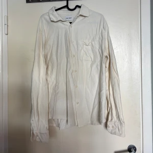 Ljusbeige långärmad skjorta från East West - Ljusbeige skjorta från East West i storlek M. Skjortan har lång ärm, knappar framtill och en bröstficka. Perfekt för en clean och stilren look. Materialet känns mjukt och bekvämt, lite åt det tjockare hållet. Funkar att använda som ovetshirt en varm sommardag.                               
