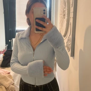 Ljusblå ribbad kofta med dragkedja - Säljer en ljusblå ribbad kofta med dragkedja framtill och stor krage. Tröjan har långa ärmar med extra långa muddar och är i ett mjukt, stickat material. Perfekt för lager-på-lager och en chill look.