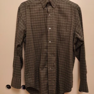 Grön rutig skjorta från Banana Republic - Säljer en grön långärmad skjorta från Banana Republic i 100% bomull. Skjortan har ett rutigt mönster i vitt, klassisk krage och knäppning framtill. Perfekt för dig som gillar en avslappnad och stilren look.