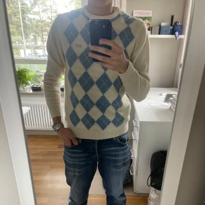 Vit och ljusblå stickad tröja med rutor - Säljer en vit stickad tröja med ljusblått argylemönster. Tröjan har rund halsringning och långa ärmar. Perfekt för dig som gillar klassisk stil med en twist.