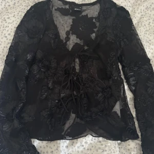 Svart blommig blus  - Säljer en svart blus från Gina Tricot instorlek XS. Blusen har svarta blommiga detaljer och har även 3 st knyt rosetter som går att knyta upp!💗Använd 1 gång!!