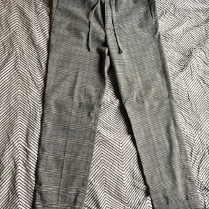 Rutig slim fit byxa från H&M - Snygga slim fit byxor från H&M i svartvitt rutigt mönster. Byxorna har dragsko i midjan och bakfickor med knapp. Perfekta för en clean och stilren look, passar till sneakers eller boots.