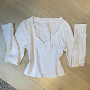 Vit långärmad v-ringad tröja - Säljer en enkel och stilren vit långärmad tröja med v-ringning. Tröjan har en figurnära passform som passar perfekt till jeans eller kjol. Perfekt basplagg för garderoben!