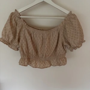 Blus från NA-KD - Supersöt croppad topp från NA-KD i beige bomull med broderade blommor. Offshoulder-modell! Använd 1-2 gånger