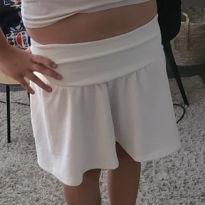 Vit kortkjol med bred midja - Superfin vit kortkjol med bred, mjuk midja och lätt utställd passform. Kjolen är enkel och stilren, perfekt för dig som gillar en clean look. Materialet känns mjukt och skönt mot huden och ger en avslappnad vibe.