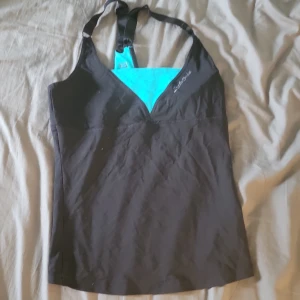 Svart linnetopp med tillhörande byxa från Better Bodies - Sportig svart linnetopp från Better Bodies med justerbara axelband och turkos detalj vid bysten. Toppen har en v-ringad skärning och är perfekt för träning. Materialet är mjukt och följsamt, vilket ger en bekväm passform. Med tillhörande träningsbyxor.