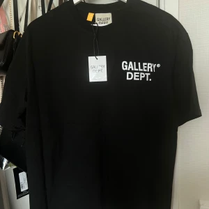 Svart t-shirt från Gallery Dept. - Svart t-shirt från Gallery Dept. med vit logga tryckt på bröstet och stor text på ryggen. Klassisk rund hals och korta ärmar. Tillverkad i mjuk bomull för en skön känsla. Perfekt för dig som gillar streetwear och enkel stil. Storleken är S men är dock oversized så passar dig som normalt vist bär M. Det bara skriva om du vill ha fler bilder och priset kan alltid diskuteras. Skickas inom 1-2 dagar.