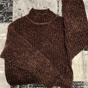 Brun ribbad från H&M Divided - Mysig brun björntröja från H&M Divided i ribbad sammet. Tröjan har hög krage, lång ärm och loose fit. Perfekt för lager-på-lager och ger en cool vintagekänsla. Materialet är mjukt och glansigt, vilket gör den extra skön att bära.