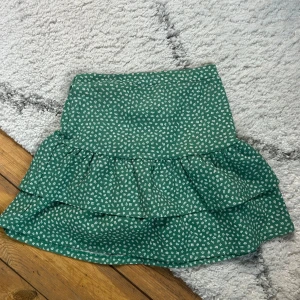 Grön blommig volangkjol Divided - Supersöt grön kortkjol från Hm med små vita blommor och volangdetaljer. Kjolen har en bekväm midja och är perfekt för vår och sommar. Snygg att matcha med en enkel topp och sneakers.