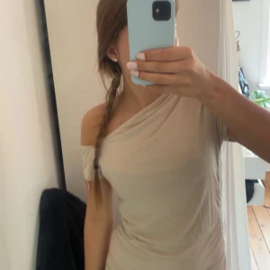 Beige offshoulder kortklänning - Snygg beige offshoulder-design och lätt rynkade detaljer längs sidan. har en tight passform och är tillverkad i mjuk bomull, perfekt för en trendig och avslappnad look.
