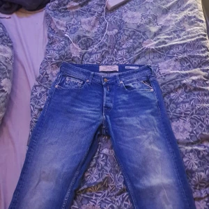 Blå jeans från Replay - Snygga blå jeans från Replay med klassisk femficksdesign och tydliga slitningar framtill. Jeansen har raka ben och detaljerade sömmar på bakfickorna. Materialet är robust denim i bomull och passformen är normal.