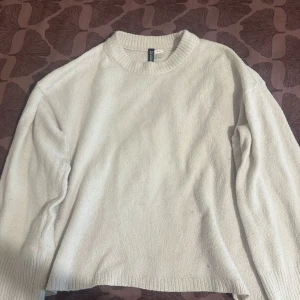 Vit stickad tröja från H&M  - En enkel och stilren vit stickad tröja från H&M.. Tröjan har rund halsringning, långa ärmar och ribbade muddar vid hals, ärmslut och nederkant. Perfekt för lager-på-lager och passar till allt i garderoben.