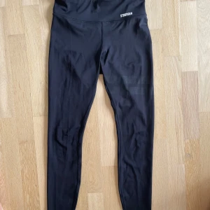 Svarta leggings från Stronger - Snygga svarta leggings från Stronger med hög midja och diskret logga framtill. Tillverkade i stretchigt material och säljer på grund av att jag har växt ut dom🩷