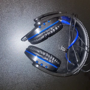 Gaming hörlurar  - Bilderna visar ett par svarta och blåa gaminghörlurar med kabel och vadderade kåpor. Perfekt för dig som gillar att lyssna på musik, spela eller streama. Hörlurarna har en modern design och ser bekväma ut för långa sessioner. Passar både ungdomar och unga vuxna.