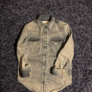 Jeansskjorta från Calvin Klein Jeans - Snygg jeansskjorta från Calvin Klein Jeans i tvättad blå färg. Klassisk westernstil med spetsig krage, två bröstfickor med lock och knappar framtill. Långärmad och tillverkad i robust denim. Perfekt för dig som gillar en avslappnad men cool look. Hör av er vid minsta fundering🙌