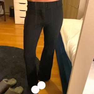 Svarta kostymbyxor med bootcut - Snygga svarta kostymbyxor med bootcut . Byxorna har klassiska fickor bak och stängs med knapp och dragkedja framtill. Perfekta för en clean och stilren look. Materialet känns mjukt och följsamt.