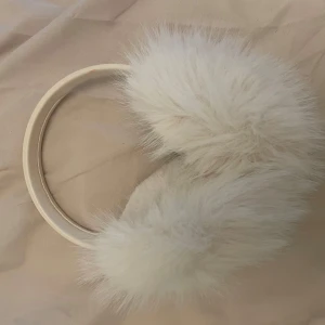 Vita fluffiga öronvärmare diadem öronmuffar  - Supermjuka och fluffiga öronvärmare i vitt med diademform. Perfekta för kalla dagar när du vill hålla öronen varma och ändå se stylish ut. Pälsimitation ger en lyxig känsla och passar till alla vinteroutfits.