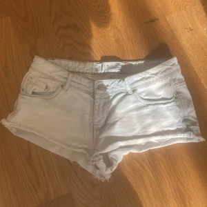 Ljusblå jeansshorts från Denim Co. - Snygga ljusblå jeansshorts från Denim Co. med råa kanter och klassisk femficksdesign. Shortsen har låg midja och är tillverkade i mjukt denimtyg, perfekta för varma dagar. Passar dig som gillar en avslappnad och trendig stil.