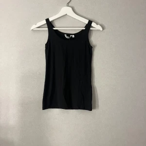 Svart linnetopp från Indiska XS - En klassisk svart linnetopp från Indiska Essentials i storlek XS. Modellen är enkel med breda axelband och rundad halsringning. Perfekt att styla med jeans eller kjol. Tillverkad i mjuk bomull som känns skön mot huden.