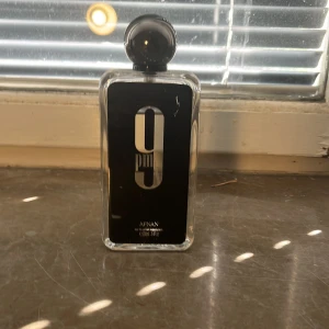 Afnan 9PM Eau de Parfum 100ml - Afnan 9PM är en parfym i en stilren, rektangulär glasflaska med svart etikett och stor rund svart kork. Parfymen kommer i en elegant svart kartong med silverdetaljer. Flaskan rymmer 100 ml och har en modern, lyxig känsla. Har använts inte så mycket men det är ungefär 85 ml kvar i flaskan.