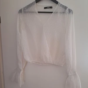 Vit prickig blus från Bik Bok XS - Superfin vit blus från Bik Bok i transparent tyg med små prickar. Omlottmodell med v-ringning och långa ärmar som avslutas med knyt och volangdetalj. Perfekt för dig som gillar romantisk och luftig stil.