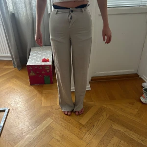 Beiga raka kostymbyxor från bershka - Snygga beiga kostymbyxor med hög midja och raka ben. Byxorna har klassisk passform, bälteshällor och stängs med knapp och dragkedja. Köpa på bershka i Spanien och ärndast använda fåtal gånger (min mamma på bilden därav lite små i midjan men passar mig som har storlek S och är 166
