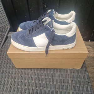 Valentino flycrewi sneakers blå/vit - Snygga Valentino flycrews sneakers i marinblå mocka och vitt skinn. Klassisk låg modell med svarta snören och coola nitar på sulan. Märkeslogga på plösen och unik sula med mönster. Perfekta för dig som vill sticka ut med stil.