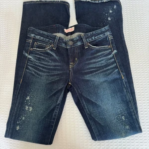 Low waisted bootcut mörkblå Moussy Vintage jeans med slitningar - Snygga mörkblå jeans från Moussy Vintage med coola slitningar och blekta detaljer framtill och på benen. Klassisk femficksmodell med kontrastsömmar och vintagekänsla. Jeansen är bootcut med låg midja. Skulle säga passar XXS/XS.