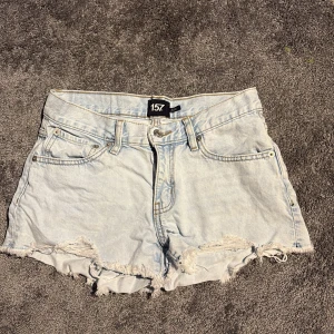 Ljusblå jeansshorts från 157 - Snygga ljusblå jeansshorts från 157 med fransiga kanter och klassisk femficksdesign. Shortsen har hög midja och slitna detaljer för en chill och trendig look. Perfekta för varma dagar och festivaler.