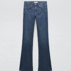 Blå bootcut jeans med låg midja - Snygga blå jeans med bootcut-silhuett och klassisk femficksdesign. Jeansen har låg midja och är tillverkade i ett mjukt denimtyg som ger en skön passform. Perfekta för dig som gillar en retrovibe och vill ha ett par jeans som sticker ut.