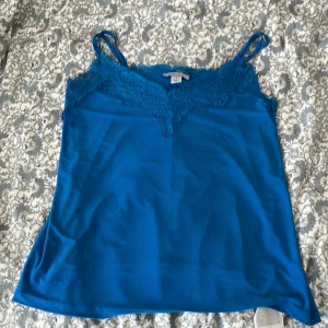 Blå linnetopp med spets från New yorker  - Supersnygg blå linnetopp  med tunna axelband och v-ringning dekorerad med spets. Med justerbara axel band🩷