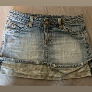 Jeanskjol med camo-detalj -  kort jeanskjol i ljusblå denim med slitningar och camouflagemönstrad kant längst ner. 