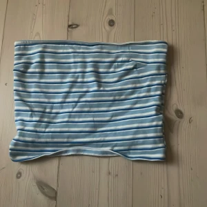 Randig tubtopp från Gina Tricot - Säljer tubtopp från Gina Tricot i storlek M. Toppen är randig i ljusblått, vitt och blått och har en gummiband för att den ska sitt uppe på insida. 