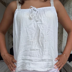 Vit linnetopp med knyt fram - Supersöt vit linnetopp med knyt fram och tunna axelband. Luftig och lätt, perfekt för varma dagar. Toppens tyg är mjukt och har en lite skrynklig struktur som ger en avslappnad vibe.