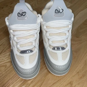Vita sneakers från Louis Vuitton - Snygga vita sneakers från Louis Vuitton med grå detaljer och märkets logotyp på sidan och baksidan. Skorna har en modern design med snörning och en bekväm passform. Perfekta för dig som vill ha stil och komfort i ett.
