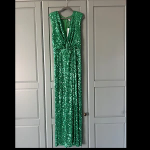 Grön paljettklänning Flavio Castellani - Snygg lång grön klänning från Flavio Castellani, täckt av glittrande paljetter. Oanvänd. Djup v-ringning framtill, ärmlös design och markerad midja. Perfekt för dig som vill sticka ut med en glamorös look.